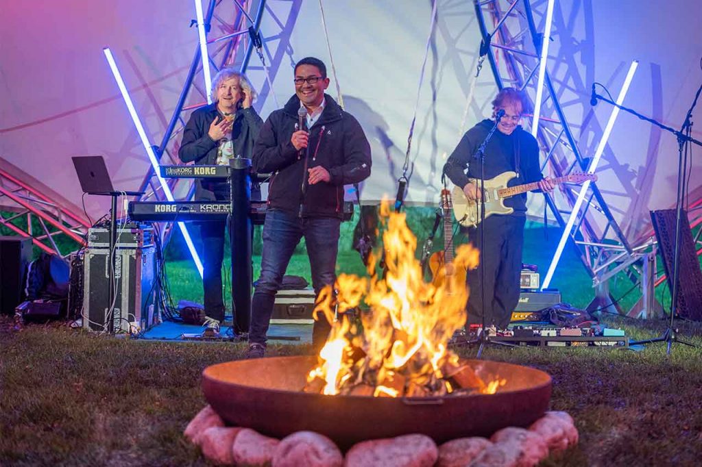 Moderator & Bandmitglieder vor einer Feuerschale bei einer Outdoor-Veranstaltung von FIREPLACE-EVENT, einem weiteren Original der FIREDANCER GmbH