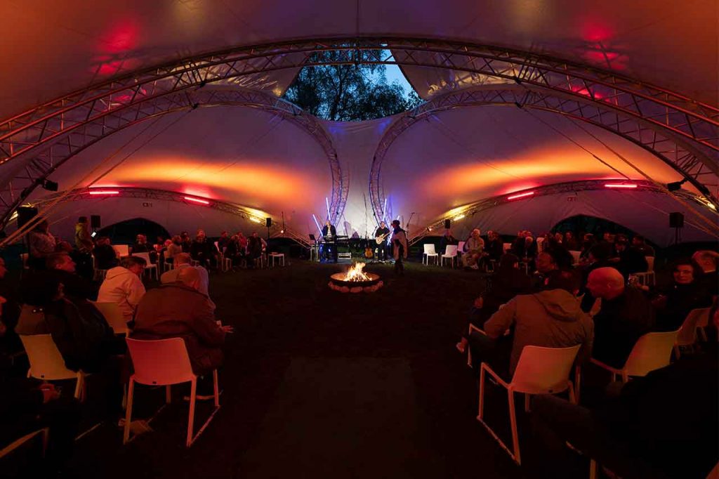 Blick in das mit Gästen gefüllte FIREPLACE-EVENT Zelt mit offenem Feuer in der Mitte bei einer Abendveranstaltung