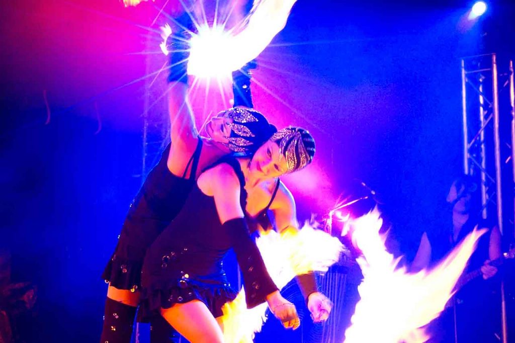 2 lächelnde Feuerkünstlerinnen Rücken an Rücken während einer FIREDANCER Feuershow